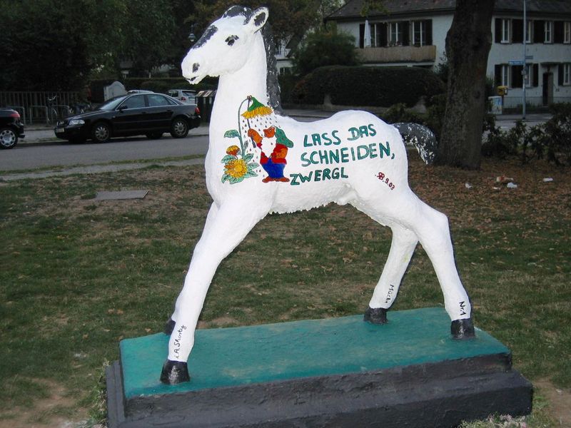 Holbein-Pferd weiß mit Gartenzwerg und Schrift „Laß das schneiden, Zwergl!“